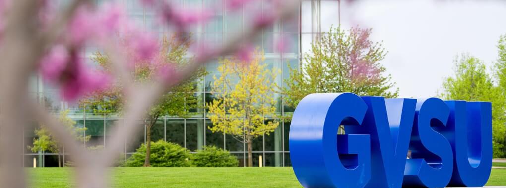 A view through blossoming tree branches of the large blue "GVSU" letters